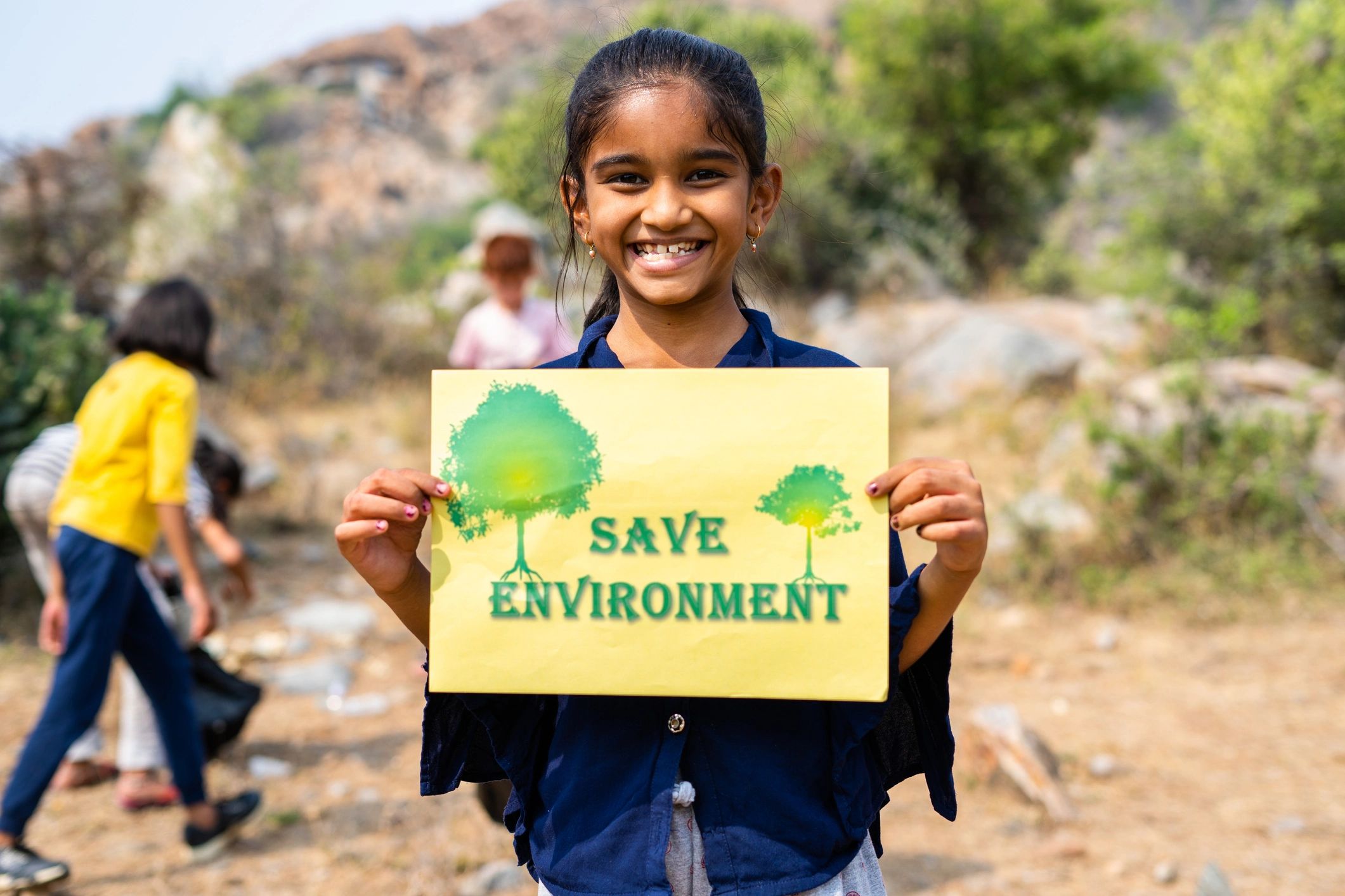 Girl holding "Save Environment" sign outdoors.